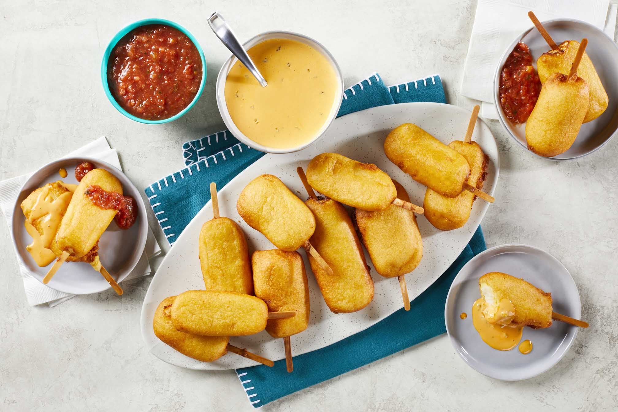 aerial shot of corn dog like queso sticks with bowl of queso and bowl of salsa